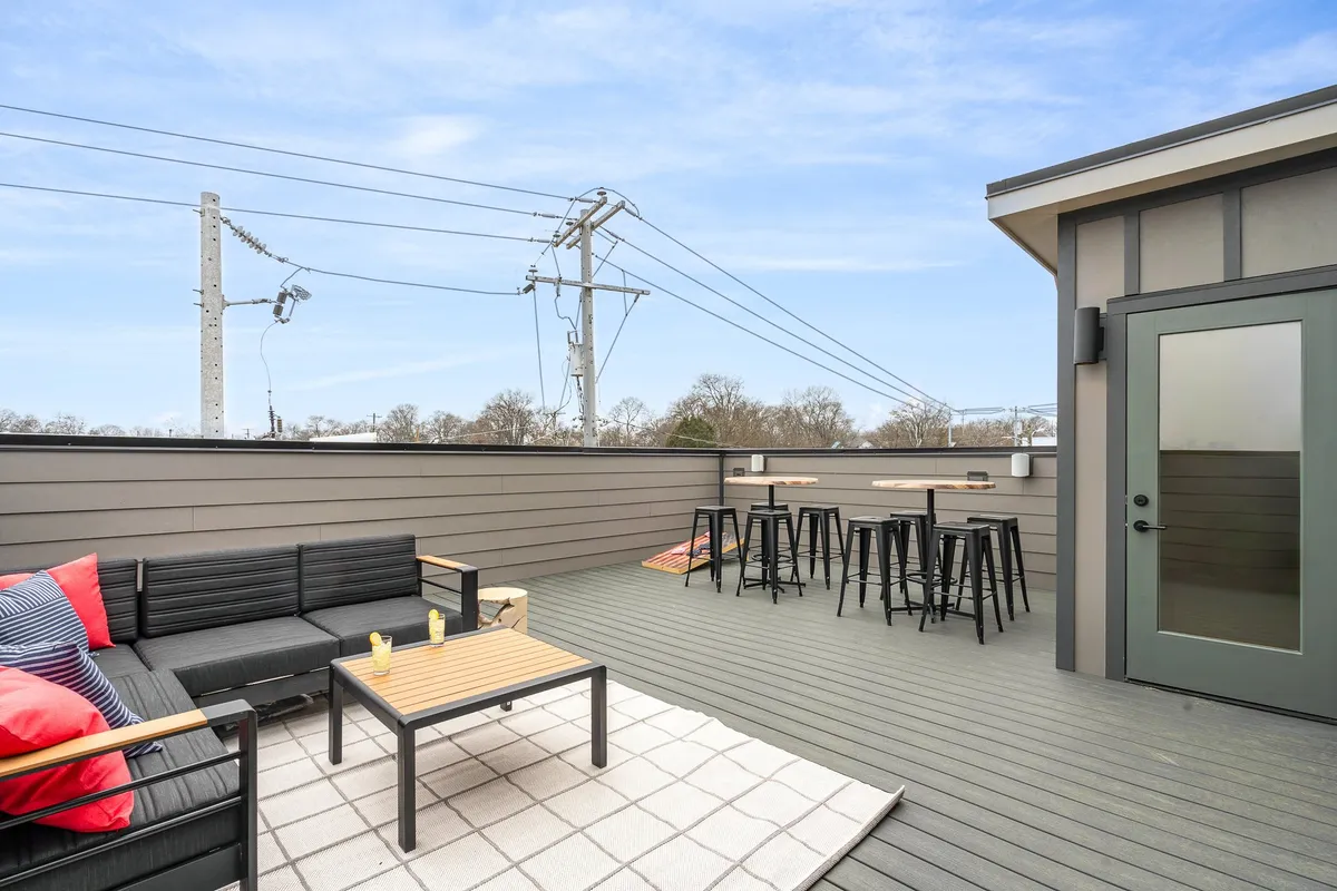A modern exterior rooftop space with a comfortable sofa seating area, bar stools, and a coffee table. The space is set for entertaining, with open views ideal for stargazing or celebrating with friends under the city lights.