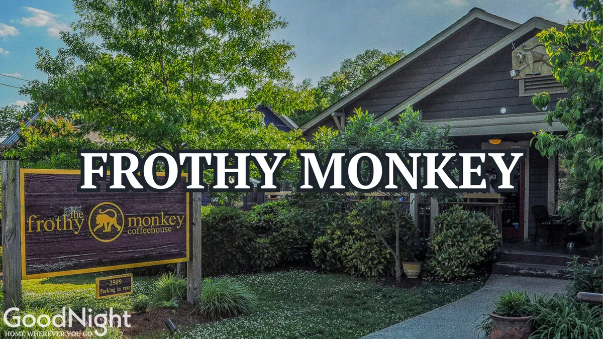 The exterior of Frothy Monkey coffeehouse, framed by leafy greenery. The inviting entrance is clearly visible, with outdoor seating and a welcoming atmosphere hinting at community and relaxation.