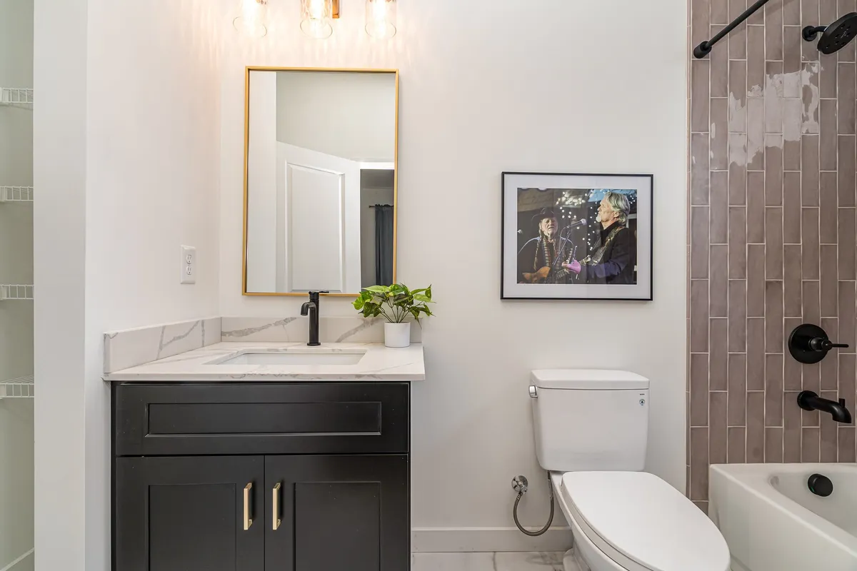 A contemporary bathroom featuring a vanity with black cabinetry, a large mirror, framed artwork, and a touch of greenery from a small plant. The overall mood is serene and functional, with ample space for personal care routines.