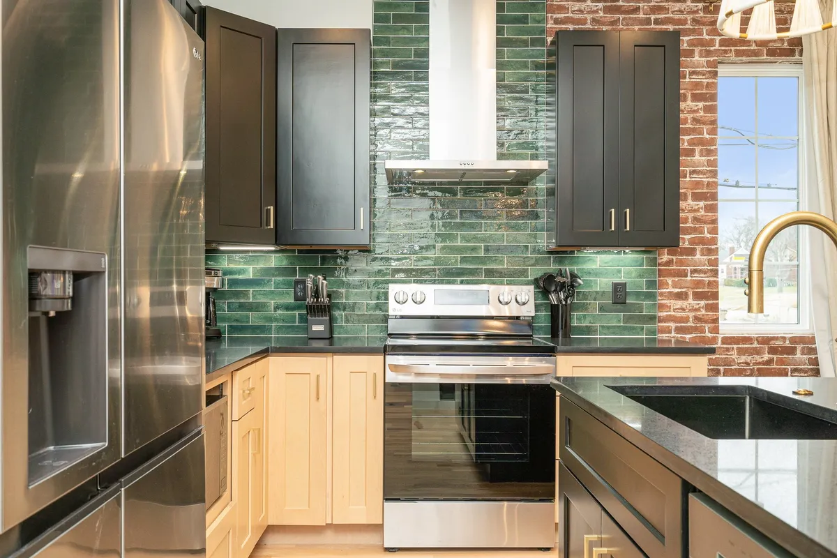 A modern kitchen featuring a striking green tile backsplash, black cabinetry, stainless steel appliances, and a gold faucet. The layout is perfect for preparing meals or gathering with friends and family.