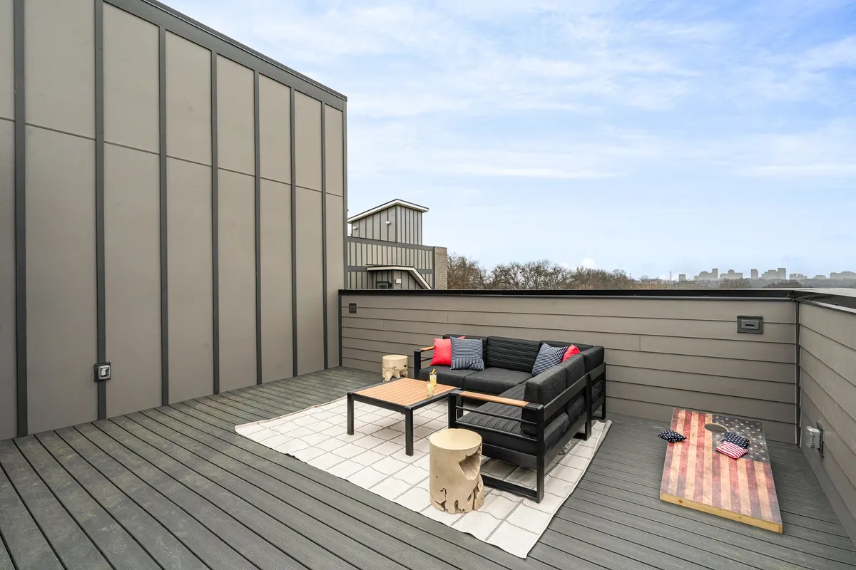 A casual and relaxed rooftop outdoor seating area featuring a coffee table, wooden stump, and decorative American flag. The setup suggests a cozy spot for morning coffee or a quiet evening, with views over the city and space for small gatherings.