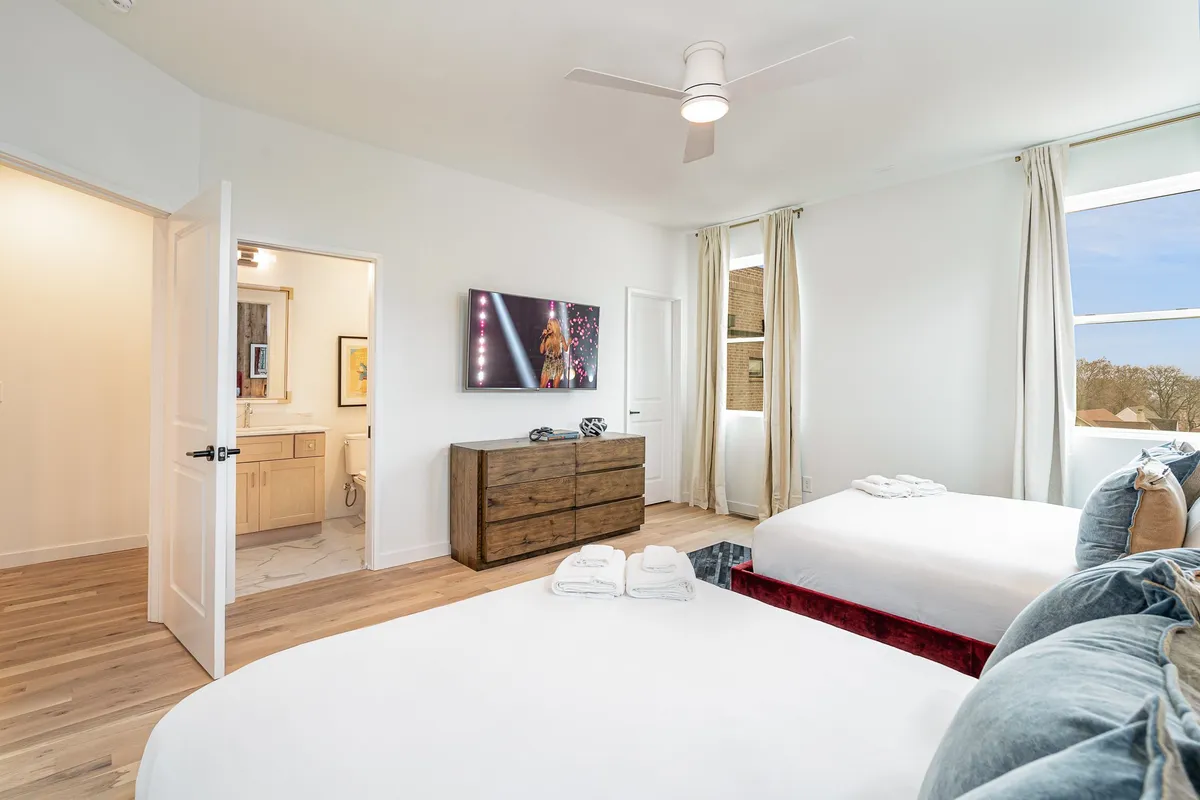 This bedroom scene features two beds, a television, a wooden dresser, and a window with curtains allowing in natural light. The space feels relaxed and functional, perfect for families or groups traveling together.