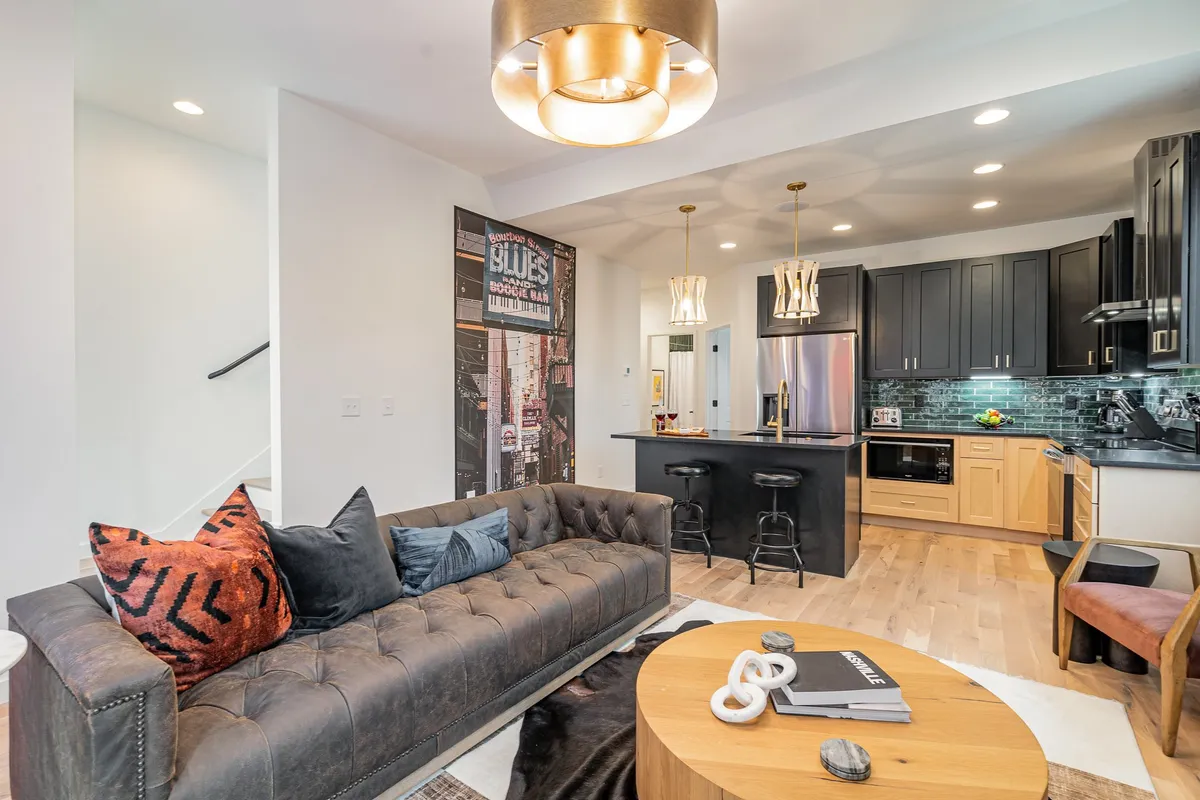 A stylish open-concept living area with a chic sofa, modern kitchen, decorative wall art, and contemporary lighting fixtures. The space exudes a sense of welcome and comfort, ideal for gatherings or quiet relaxation.